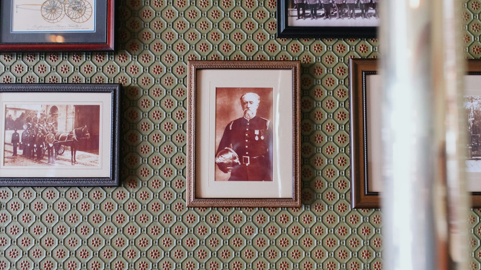 Framed sepia portraits and pictures on a patterned green wall.