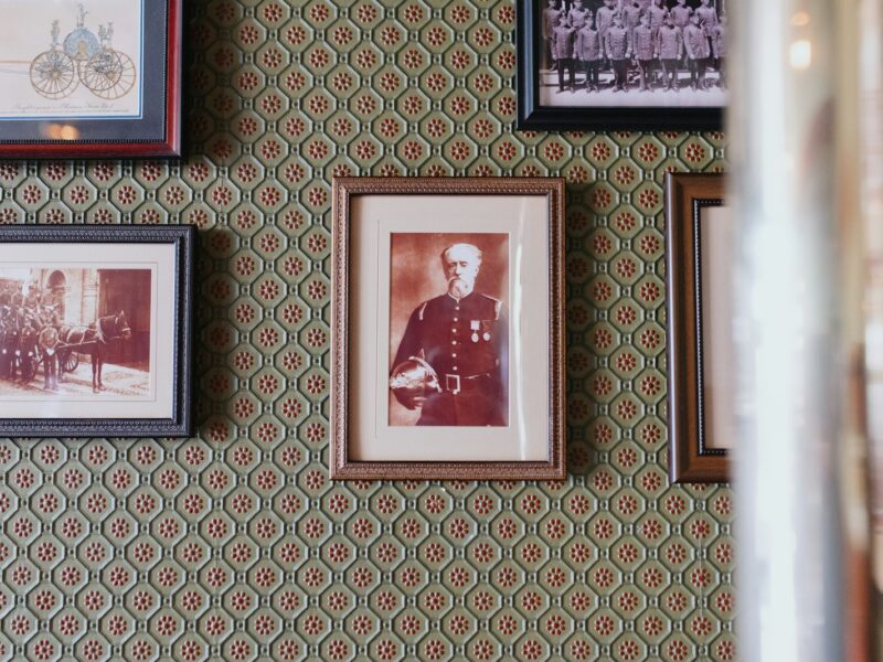 Framed sepia portraits and pictures on a patterned green wall.