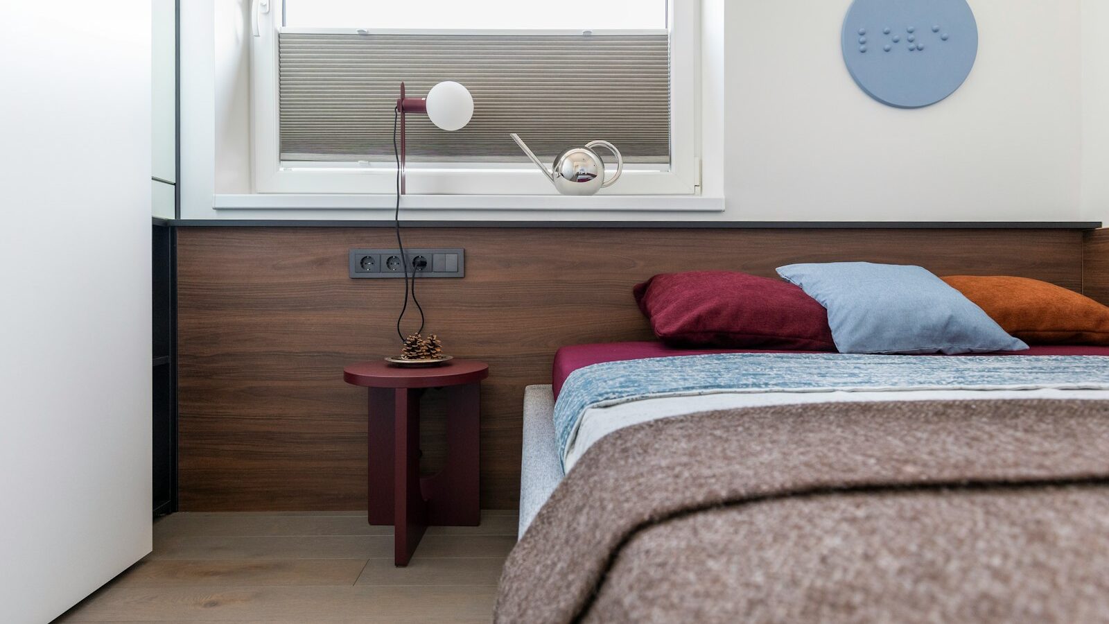 Modern bedroom with colorful bedding, wooden headboard, and minimalist lamp.