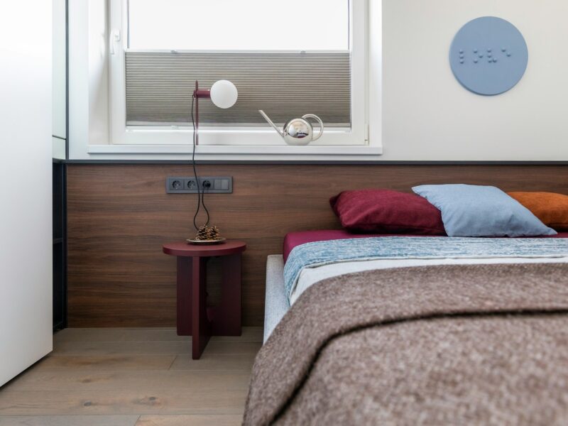 Modern bedroom with colorful bedding, wooden headboard, and minimalist lamp.
