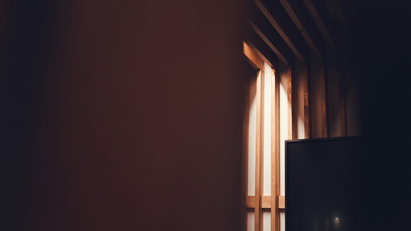 Narrow light beam entering a dark room with wooden slats.
